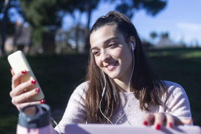 Smiling young woman using mobile phone while listening music