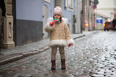 Girl eating lollipop while standing on street in city