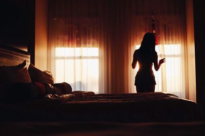 Rear view of woman standing by curtain in bedroom