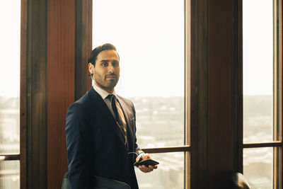 Portrait of confident financial advisor with smart phone against window at law office