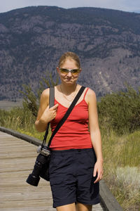 Portrait of young woman standing on boardwalk against mountain
