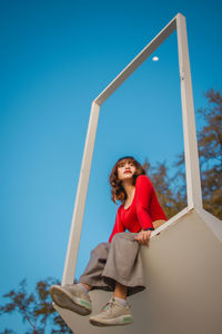 Low angle view of young woman holding umbrella against blue sky