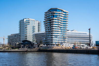 Modern buildings by river against sky in city