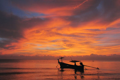 Silhouette boat moored on sea against orange sky