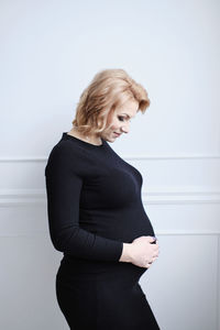 Pregnant woman in black dress smiling touching tummy