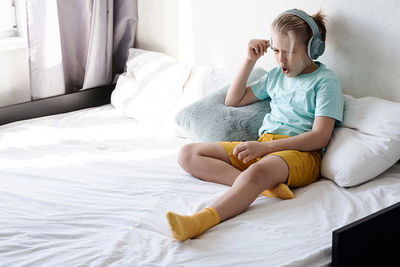 Cute boy listening to music in earphones seating on bed. child wearing headphones listens to music.