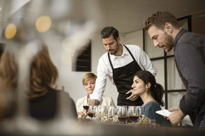 Man in apron arranging various wineglasses on table for business people