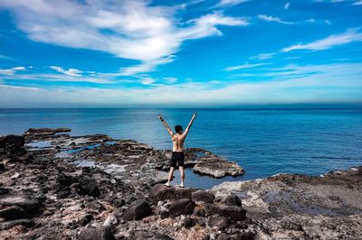 Woman standing on rocks by sea against sky