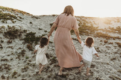 Behind view of mother walking toddler twins in sand to go to the ocean