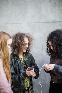 Happy friends charging mobile phone against wall