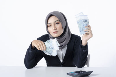 Portrait of young woman holding camera over white background