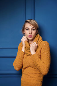 Portrait of young woman standing against blue wall