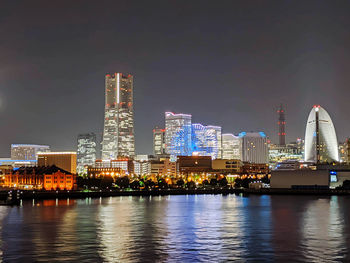 Illuminated city by river against sky at night