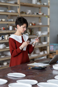 Young woman ceramic studio owner managing small business finances, doing pottery cost analysis