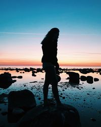 Silhouette man standing on rock at beach against sky during sunset