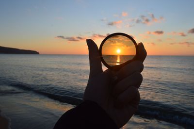 Person hand holding sun at beach during sunset