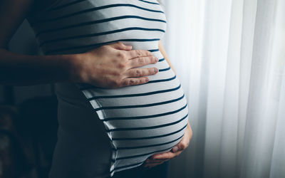 Midsection of pregnant woman standing at home