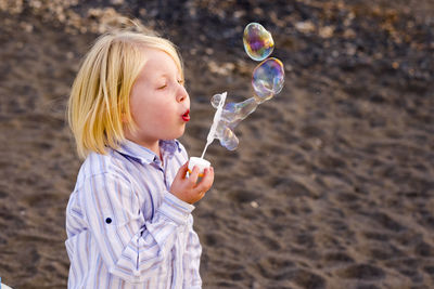 Boy blowing bubbles while standing at beach