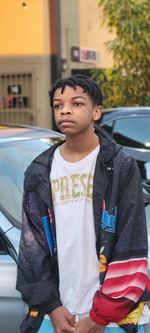 Side view of young man standing by cars