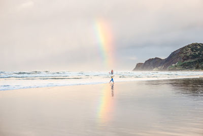 Girl running on a beach under a rainbow near a mountain