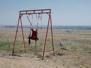 Swing on field by sea against sky