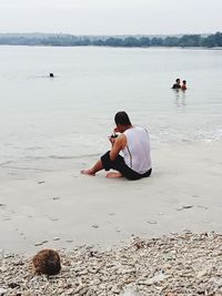 Rear view of man sitting on shore at beach