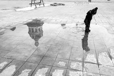 Boy standing on puddle with reflection of building on pavement