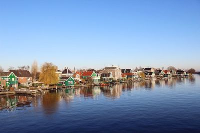 Buildings by river against clear blue sky