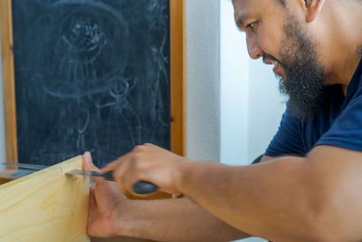 Bearded asian carpenter using hand saw cutting wooden boards