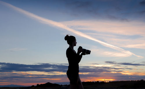 Silhouette woman photographing against sky during sunset