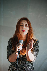 Portrait of redhead female singer woman in sparkly evening dress holding microphone on dark night