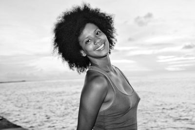 Portrait of smiling young woman standing at beach against sky