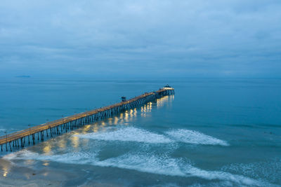 Drone view of imperial beach pier at dawn. waves break against the structure.