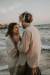 Young couple standing at beach against sky