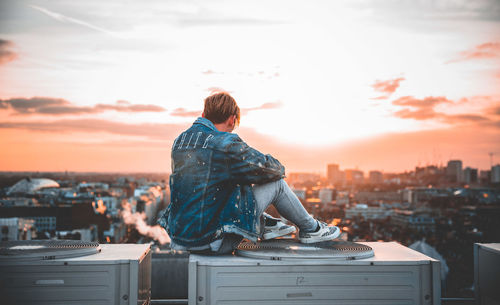 Rear view of man looking at cityscape against sky during sunset