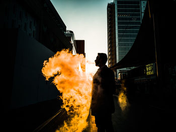 Double exposure of man standing by fire with city in background