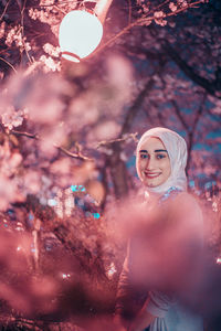 Portrait of smiling young woman standing by cherry blossom