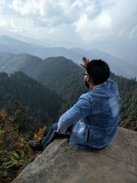 Man sitting on mountain against sky