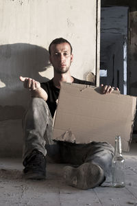 Portrait of young man sitting against wall