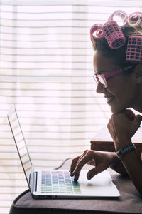 Side view of woman with hair curlers using laptop at home