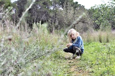 Girl crouching on grassy field against trees