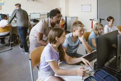 Male and female teacher assisting students in computer class at school