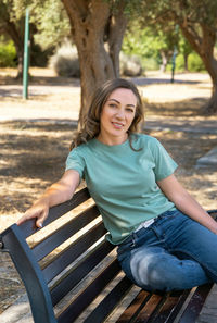 Portrait of young woman sitting on bench at park