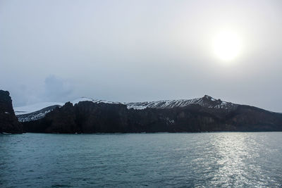 Scenic view of sea by snowcapped mountains against sky