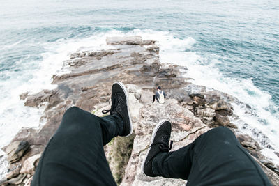 Low section of man sitting on cliff against sea