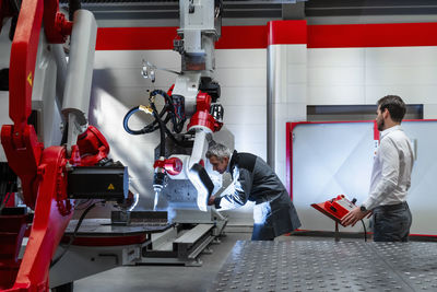 Mature man with welding helmet examining robotics in factory