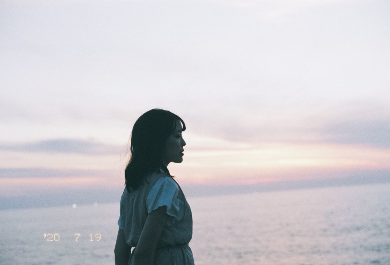 YOUNG WOMAN STANDING BY SEA AGAINST SKY