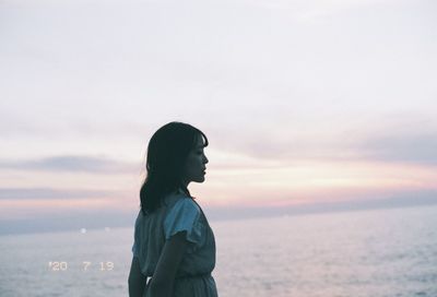 Woman standing by sea against sky during sunset