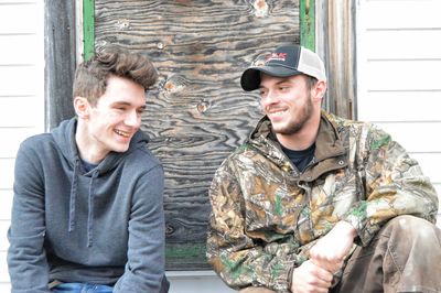 Happy young friends sitting against house with closed door