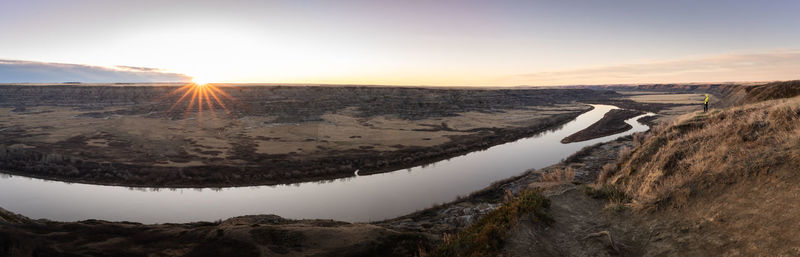 Panoramic sunrise shot of desert like canyon with river flowing through, drumheller region, canada